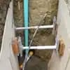 A trench with shoring equipment bracing the walls, revealing a light blue sewer pipe and other utility lines underground, indicating a repair in progress.