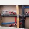 Exposed wall cavity showing new plumbing installations: black ABS drain pipes, red and blue PEX water lines connected to copper stub-outs, and wooden framing.