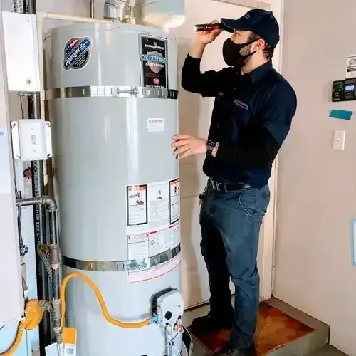 A technician in a dark uniform and face mask inspects a Bradford White water heater with a flashlight in a utility room.